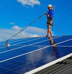 Technican using water fed pole system to cleaning solar panels ontop of a roof